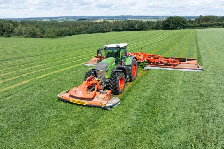 Tracteur agricole Fendt vert avec combiné de fauche Kuhn Conviva frontal et arrière, fauchant une prairie verte lors d'une journée ensoleillée, vue aérienne.